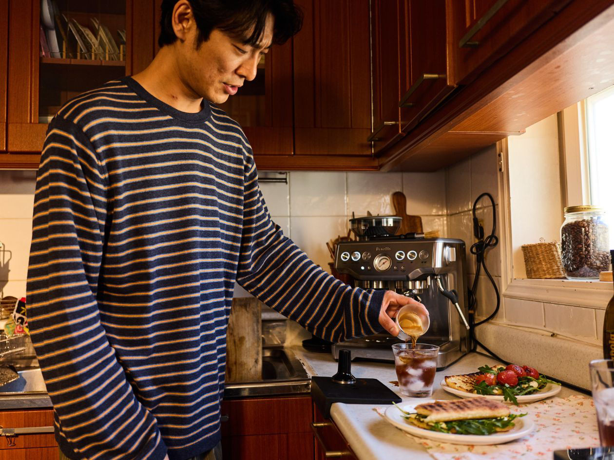 Person in striped shirt prepares food at a kitchen counter and pouring coffee in glass full of ice
